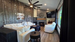 A modern living room with a fireplace, a large clock, and a television. - Mississippi River view. Duck Hunters Get away. 4 Bedroom, 5 bed - Sleeps 10. (Brownsville)