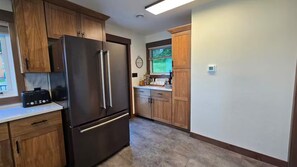 A kitchen with wooden cabinets, a stainless steel refrigerator, and a window with a view of greenery.