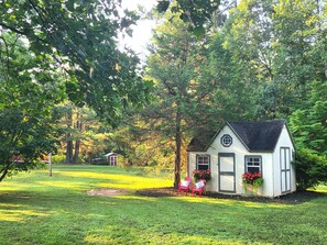 Une petite maison blanche avec un toit noir, entourée d’arbres et d’herbe d’un vert luxuriant.