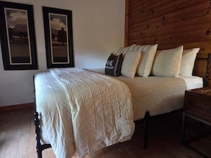 Une chambre à coucher avec une tête de lit en bois, un lit recouvert d’une couette blanche, plusieurs oreillers et deux tableaux encadrés accrochés au mur.