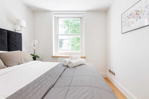 Ein Schlafzimmer mit einem Bett, einem Fenster, einer Pflanze und einem Bild an der Wand.