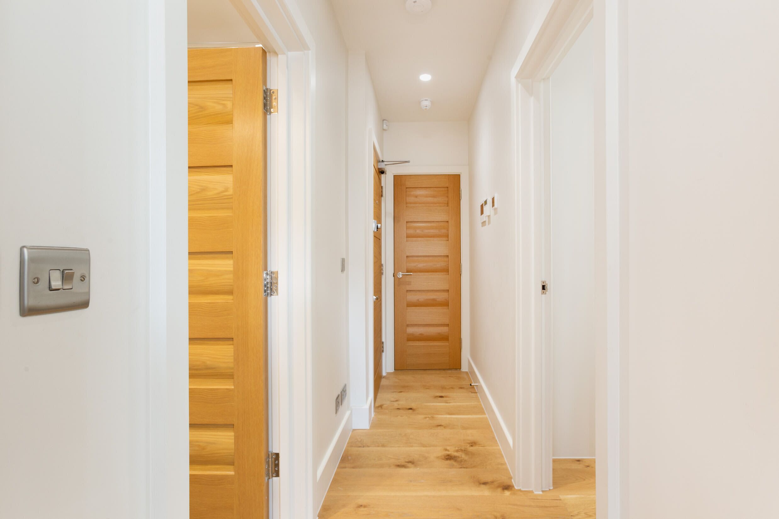Un pasillo estrecho con suelo de madera y paredes blancas, que conduce a una puerta con un diseño de panel de madera.
