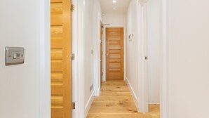 A narrow hallway with wooden flooring and white walls, leading to a door with a wooden panel design. - Chic 1BR Fitzrovia Apartment by Bloomsbury (London)