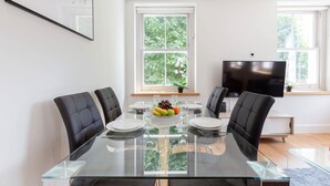 A modern dining area with a glass table, black chairs, and a fruit bowl. - Chic 1BR Fitzrovia Apartment by Bloomsbury (London)