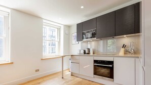 A modern kitchen with white cabinetry, a built-in oven, and a microwave. - Chic 1BR Fitzrovia Apartment by Bloomsbury (London)