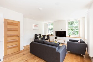 Ein modernes Wohnzimmer mit einer Couch, Sesseln, einem Fernseher und einem Essbereich mit Tisch und Stühlen.