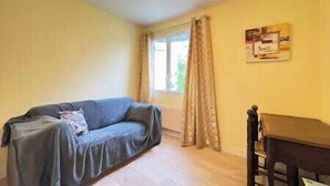Ein Zimmer mit Sofa, Tisch, einem Fenster mit Vorhängen und einem an der Wand befestigten Schild.
