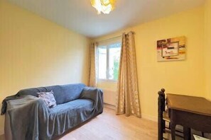 A room with a sofa, a table, a window with curtains, and a wall-mounted sign. - Les Sylphes - Parking, WiFi, TV, 350m to the beach (Pornichet)
