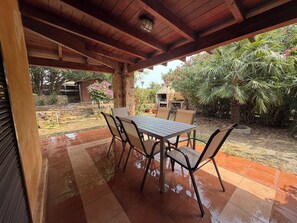 An outdoor patio with a table and chairs, surrounded by a garden with various plants and a small structure. - Villa Aurea House with Garden, Vico Andrea Doria Bassa 8 (Costa Rei)