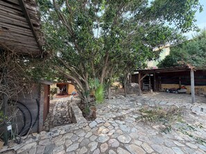 A courtyard with stone paving, a wooden structure, and a tree providing shade. - Villa Aurea House with Garden, Vico Andrea Doria Bassa 8 (Costa Rei)