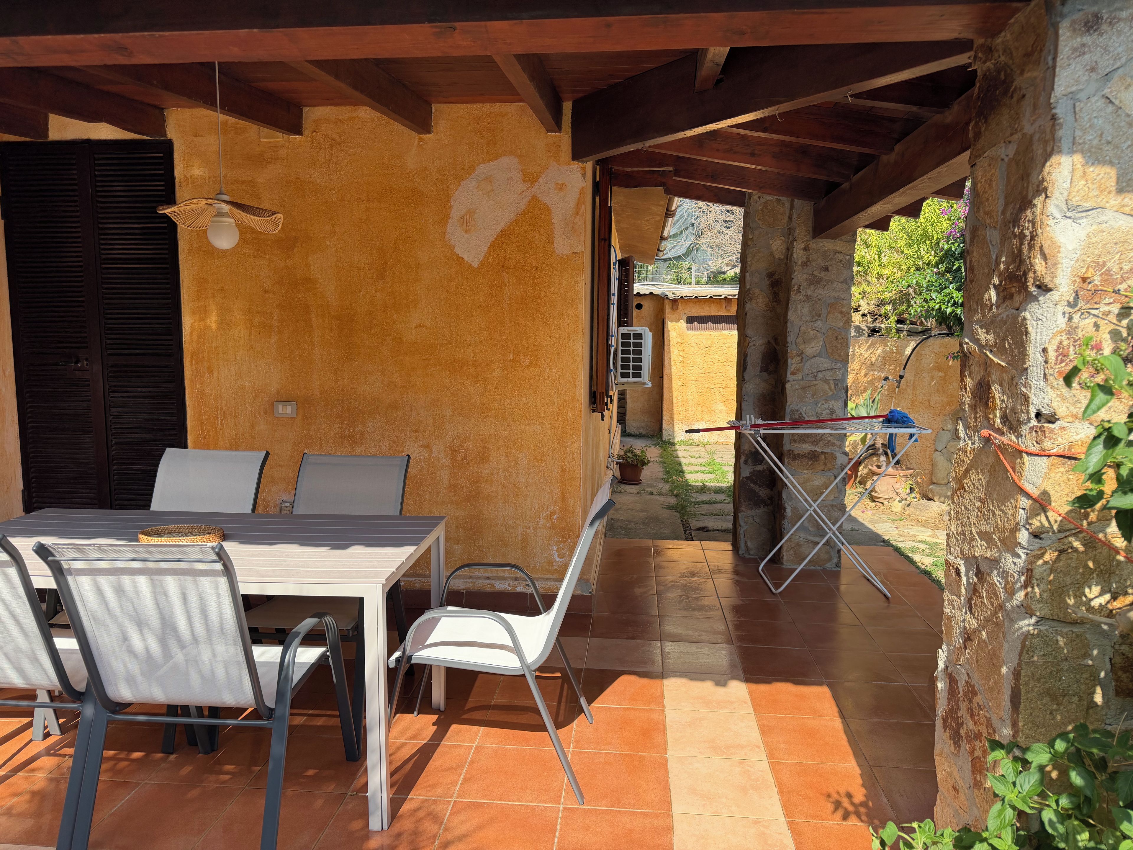 Eine Terrasse im Freien mit Tisch und Stühlen, einer hängenden Leuchte und einer Steinmauer.