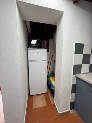 A compact kitchen with a white refrigerator, a microwave on top, and a tiled backsplash. - Villa Aurea House with Garden, Vico Andrea Doria Bassa 8 (Costa Rei)