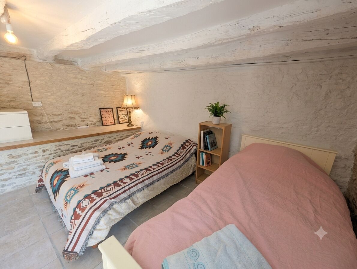 A bedroom with a bed, bedside table, lamp, and a wall-mounted shelf with books and a plant.