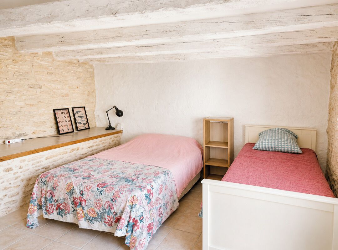 Ein Schlafzimmer mit zwei Betten, einem Holzregal, einer Lampe und einer Steinwand.