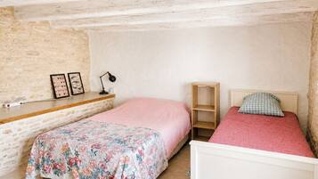 Ein Schlafzimmer mit zwei Betten, einem Holzregal, einer Lampe und einer Steinwand.