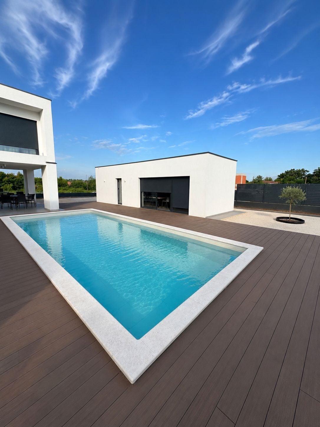 Ein rechteckiger Swimmingpool mit weißer Umrandung, umgeben von einer Holzterrasse.