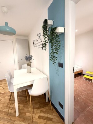 A modern dining area with a white table and chairs, a potted plant, and a wall-mounted light fixture. - Principino - Walk to the Old Port and the Aquarium; take the train to the Cinque Terre. (Genova)
