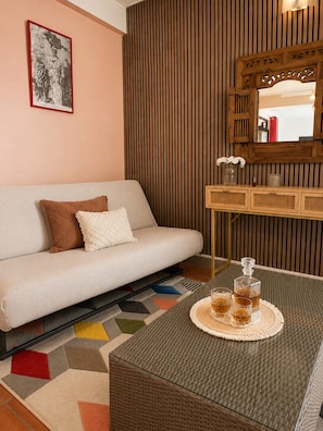 Ein modernes Wohnzimmer mit einer Couch, einem Couchtisch mit Getränken, einem Spiegel und einem gerahmten Bild an der Wand.