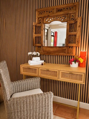 Ein Zimmer mit einem Holzanrichte, einem Korbstuhl und einem Spiegel mit verziertem Holzwerk.