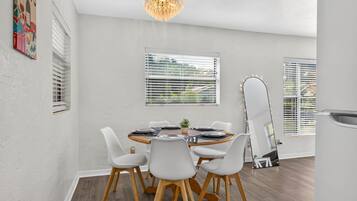 A dining area with a round table, white chairs, and a chandelier.