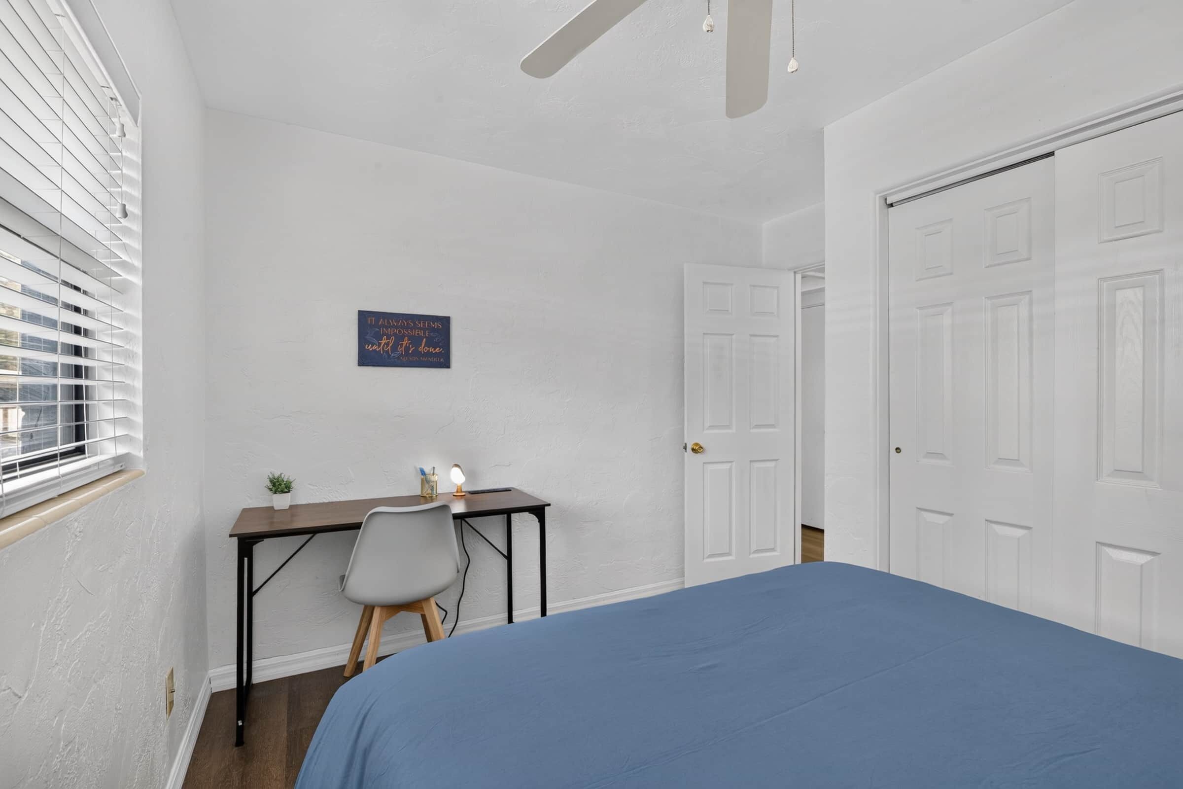 A bedroom with a bed, a desk, a chair, and a door.