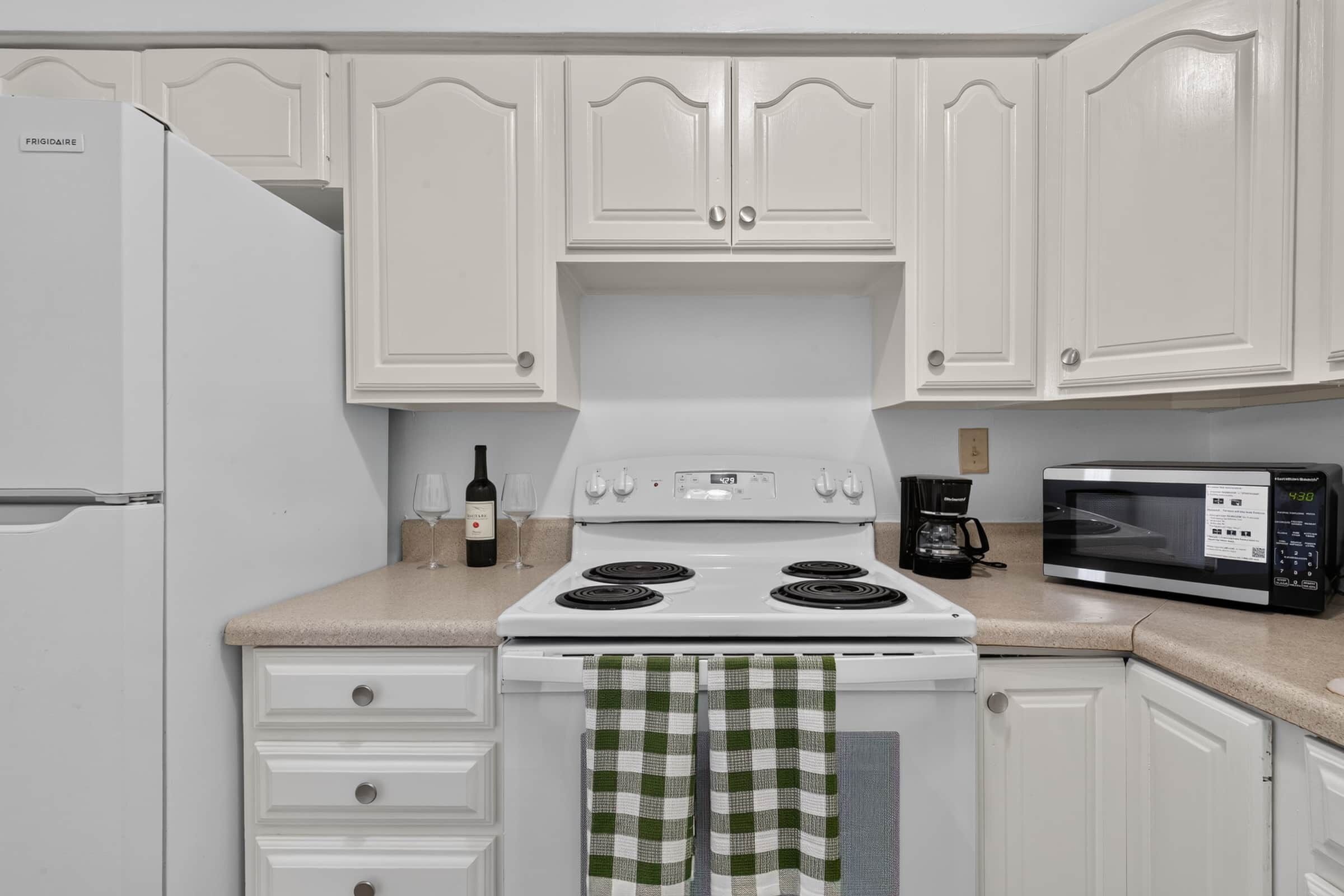 A kitchen with white cabinetry, a white stove, a microwave, and a refrigerator.
