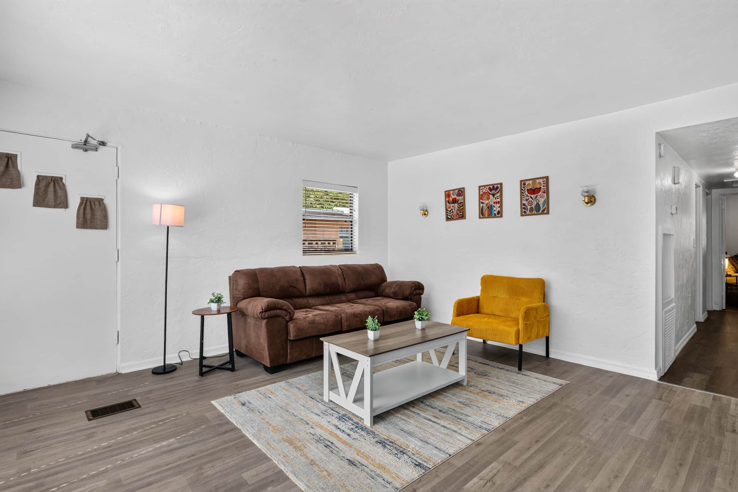 Ein Wohnzimmer mit einem braunen Sofa, einem gelben Sessel, einem Couchtisch und einem Teppich mit Muster.