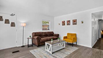 Ein Wohnzimmer mit einem braunen Sofa, einem gelben Sessel, einem Couchtisch und einem Teppich mit Muster.