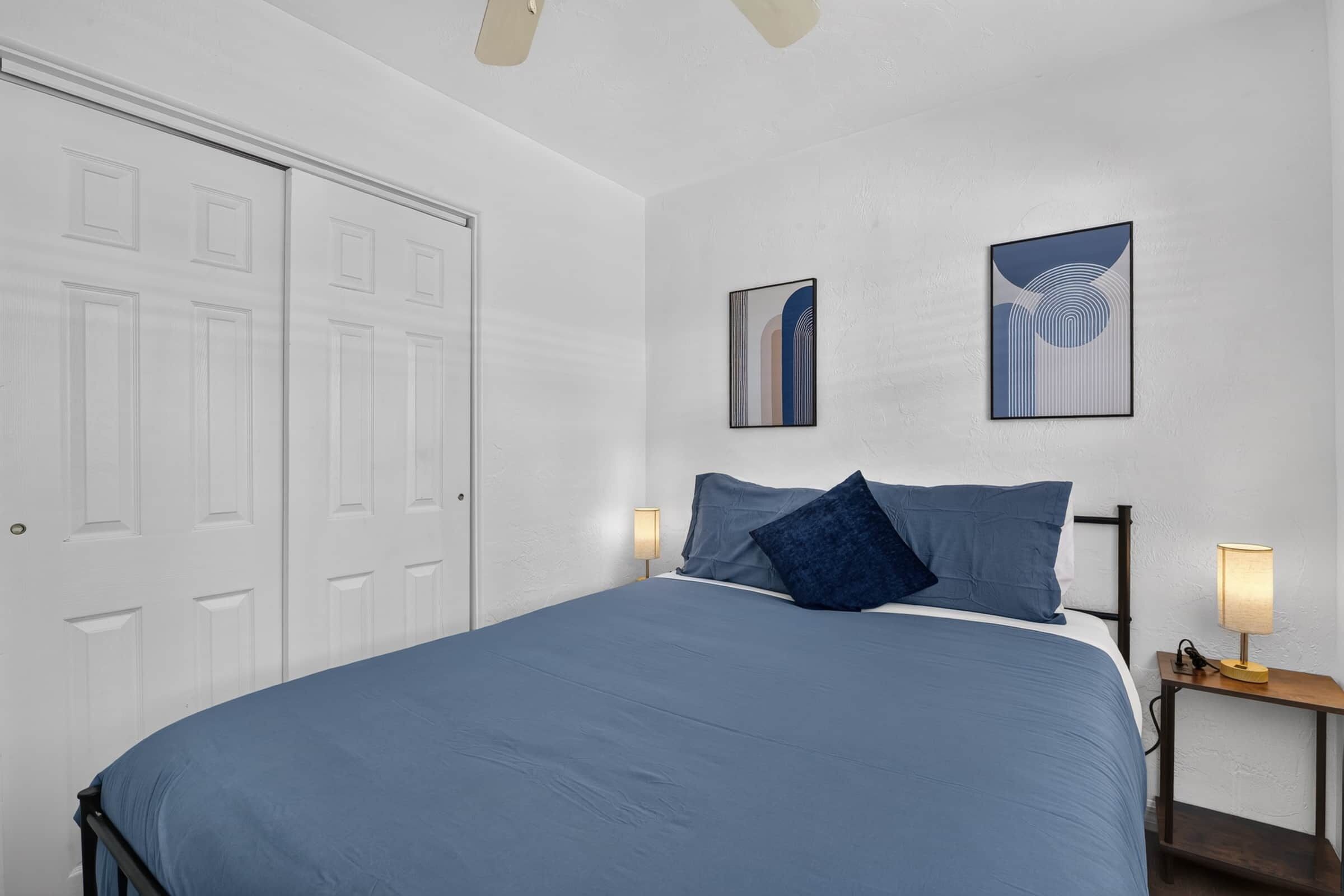 A bedroom with a bed, two bedside lamps, and two framed artworks on the wall.
