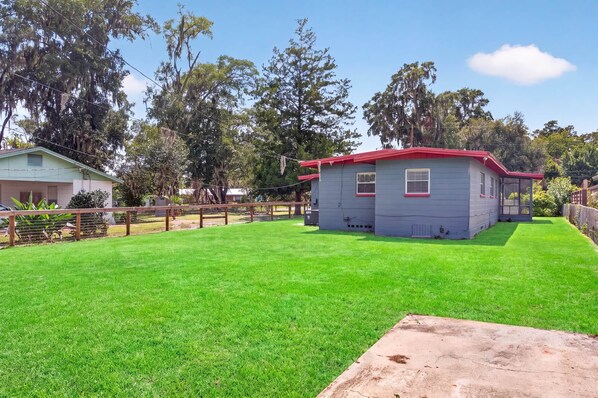 A small, single-story house with a red roof and a fenced yard.