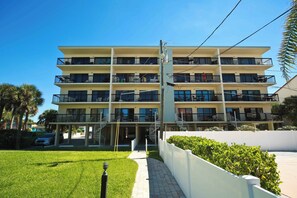 A multi-story hotel with balconies, a central staircase, and a well-maintained lawn. - Top Floor Gulf Front • Pool • Sand Castle North 503 (Indian Rocks Beach)