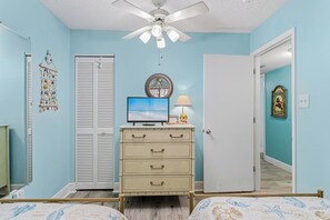 A bedroom with a bed, a dresser, a television, a ceiling fan, and a door. - Top Floor Gulf Front • Pool • Sand Castle North 503 (Indian Rocks Beach)