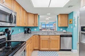 A kitchen with wooden cabinets, a microwave, stove, and dishwasher. - Top Floor Gulf Front • Pool • Sand Castle North 503 (Indian Rocks Beach)