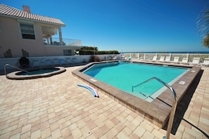 A swimming pool with a view of the ocean, a covered area with lounge chairs, and a building with a balcony. - Top Floor Gulf Front • Pool • Sand Castle North 503 (Indian Rocks Beach)