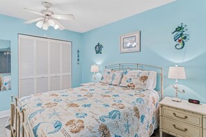 Une chambre à coucher comprenant un lit, une table de chevet, des œuvres d’art murales et un ventilateur de plafond.