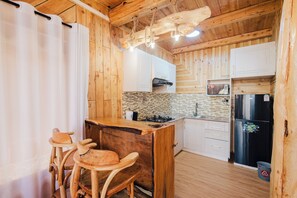 A wooden kitchen with a central island, bar stools, a stove, and a refrigerator.