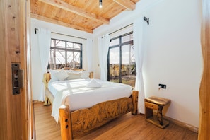 A bedroom with a wooden bed, large windows, and a view of the outside.