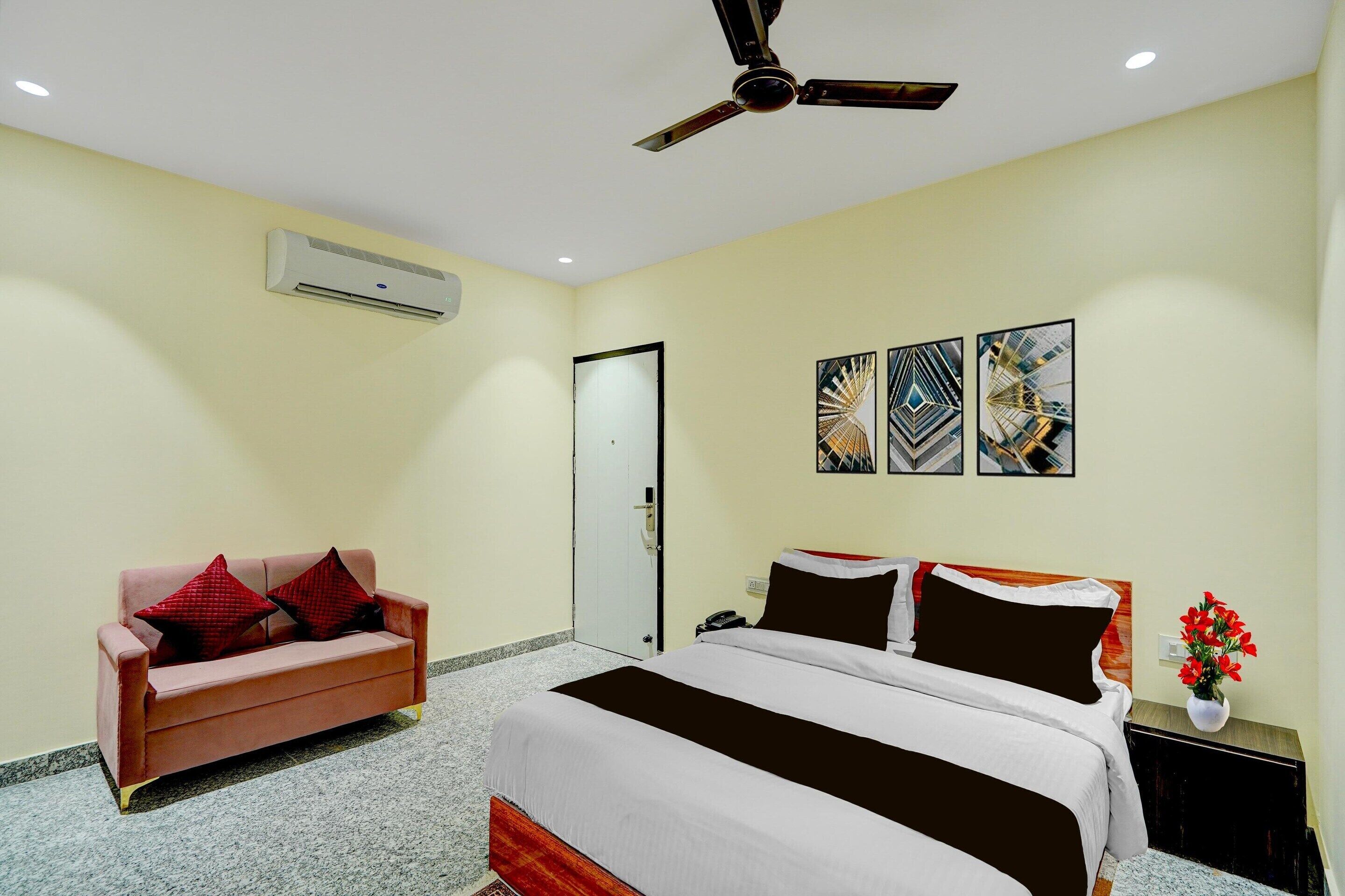 Habitación de hotel con cama, sofá, aire acondicionado, ventilador de techo y tres obras de arte en la pared.
