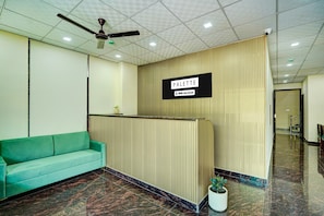 Uma área de recepção com um sofá verde-água, um ventilador de teto, uma placa com a inscrição 'PALETTE' e uma planta em vaso.
