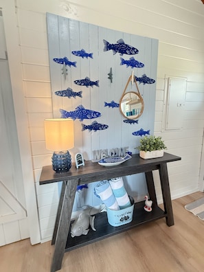 A room with a wall decorated with fish decals, a round mirror, a welcome sign, a shoe rack, and a small potted plant. - Cozy Cabin on Lake Hamilton (Mountain Pine)