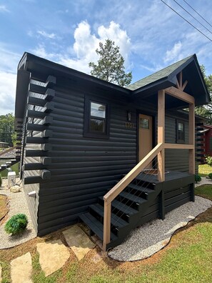 A log cabin with a wooden staircase leading to a porch, a window, and a door. - Cozy Cabin on Lake Hamilton (Mountain Pine)