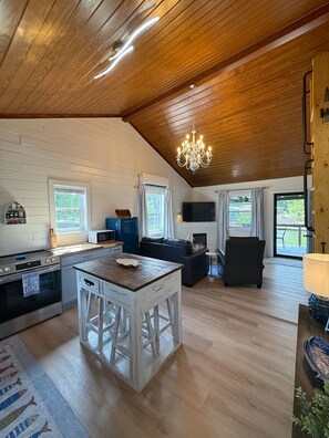 A spacious living area with a wooden ceiling, a central island with stools, a television, and a dining table. - Cozy Cabin on Lake Hamilton (Mountain Pine)