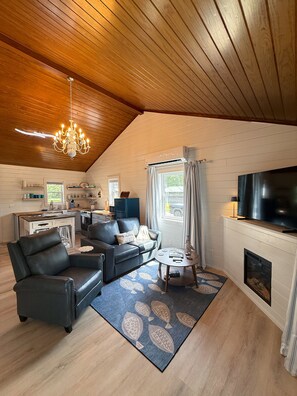 A cozy living room with a fireplace, a television, and a dining area with a kitchen in the background. - Cozy Cabin on Lake Hamilton (Mountain Pine)