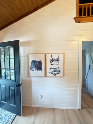 Una habitación con techo de madera, una puerta negra y dos cuadros en la pared.