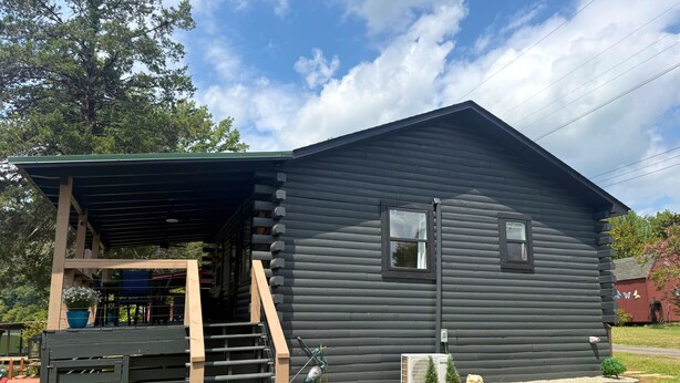 A log cabin with a covered porch, a staircase, and a welcome sign.