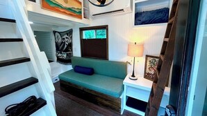 Et værelse med en grøn sofa, en lampe, et billede og en trappe.