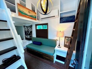 Ein Zimmer mit einem grünen Sofa, einer Lampe, einem Gemälde und einer Treppe.