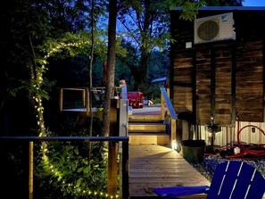 Eine Holzdielen-Terrasse mit einer Treppe zu einer Hütte, umgeben von Bäumen und einer Lichterkette.