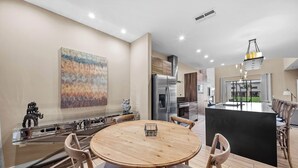 Eine moderne Küche mit einer zentralen Kochinsel, Edelstahlgeräten und einem Essbereich mit rundem Holztisch und Stühlen.