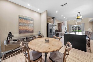 A modern kitchen with a central island, stainless steel appliances, and a dining area with a round wooden table and chairs. - 4BR house sleeps 10 in Magic Village Views (Kissimmee)